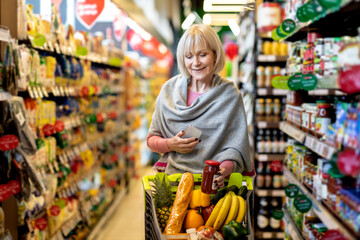 Senior woman customer using mobile phone while shopping at supermarket