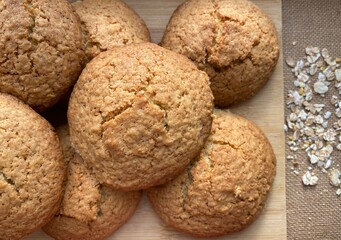 Oatmeal cookies on a wooden board. Dessert rich for breakfast for children. Brown background, top view. Oatmeal is sprinkled randomly on the table.