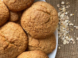 Oatmeal cookies top view. Oat flakes are scattered on the table. Brown cookies lie on burlap.