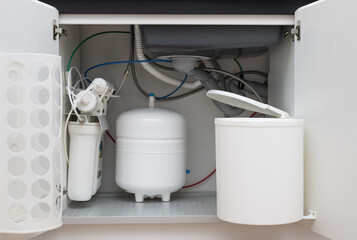 Opened kitchen cabinet with sink, installed garbage bin and house water filtration system. Kitchen...