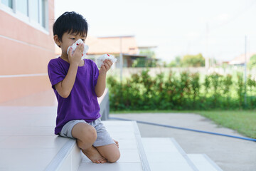 Asian boy holding blood tissue paper from nose bleeding problem