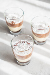 Three-layer chocolate and vanilla mousse dessert in glass cups, sprinkled with coconut flakes, on a children's serving board. brunch