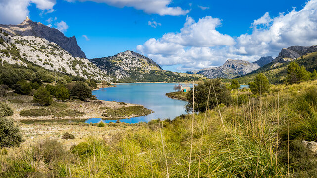 Panorama view over artificial lake Embassament de C&uacute;ber at the hiking trail GR-221 with hiking retreat Refugi de C&uacute;ber located at the grassy lake shore with mountains in the background.