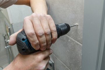 Rapairman drilling ceramic tile on a wall.