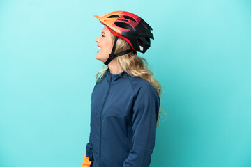 Young cyclist woman isolated on blue background laughing in lateral position