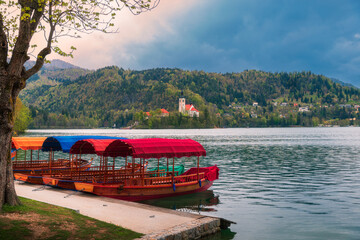 Pletna boats in Bled Lake (Slovenia) in a cloudy day. In the backgroud the insland with the Church of the Assumption of Mary and the alps covered by woods and trees