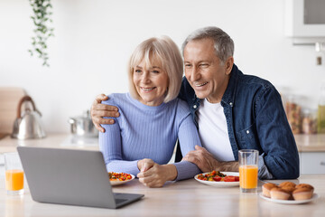Cheerful senior couple using computer while having breakfast