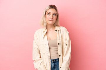 Young caucasian woman isolated on pink background having doubts while looking up