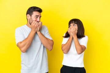 Young couple isolated on yellow background is a little bit nervous and scared putting hands to mouth
