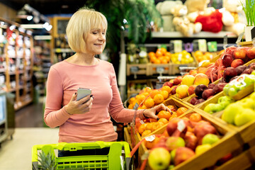 Cheerful senior lady customer purchasing at store, using phone