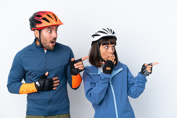 Young cyclist couple isolated on white background pointing finger to the side with a surprised face