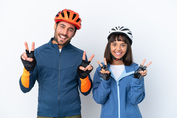 Young cyclist couple isolated on white background smiling and showing victory sign with both hands