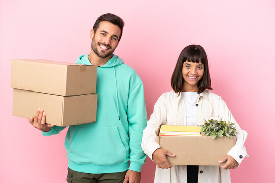 Young Beauty Couple Moving In New Home Among Boxes Isolated On Pink Background Posing With Arms At Hip And Smiling