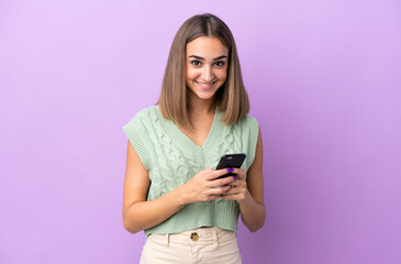 Naklejka premium Young caucasian woman isolated on purple background sending a message with the mobile
