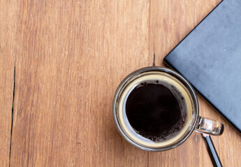 Top view of black hot americano coffee in a cup on a rustic wooden table with a book and pencil. Relax and coffee break concept