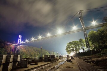 Fototapeta na wymiar Illuminated pedestrian bridge above river at night park
