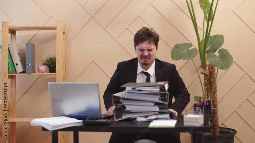 Poster male manager hysterically and angry hit head against stack of folders of documents due to stress at 
