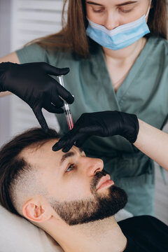 Mesotherapy for man hair. Attractive man receiving injections in his head. Man having mesotherapy session at beauty salon, therapist in protective glove with syringe, copy space