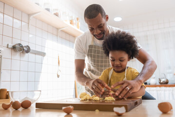 Happy Smiling African American Father teaching little Son kneading dough in kitchen, Black Family...