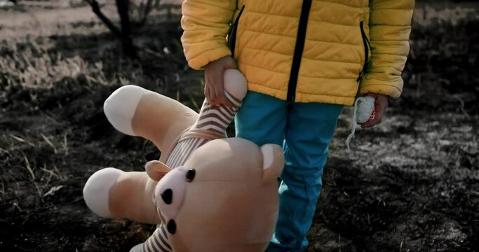 Kid in Ukrainian national colors, Sad refugee litle girl pose with a toy bear with a burnt background after the bombing. Stop War. Crisis, war conflict. stop aggression. kid homeless at war in Ukraine
