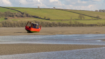 Stranded by the ebb tide, a rusting fishing trawler lays beached on a sandbank. River Teifi Estuary, with hilly farmland background. Rippling blue water. Landscape image with space for text. Wales. - 502027015