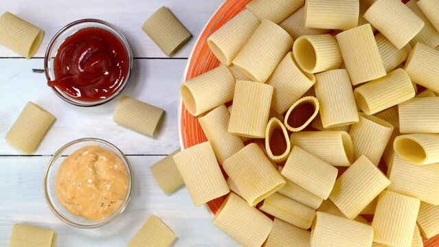 Uncooked raw italian paccheri pasta rotating slowly on turntable in dish.