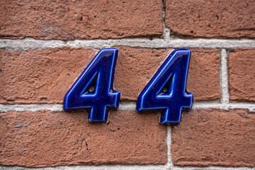 The number 44 in blue ceramic finish on red brick wall. Forty four.