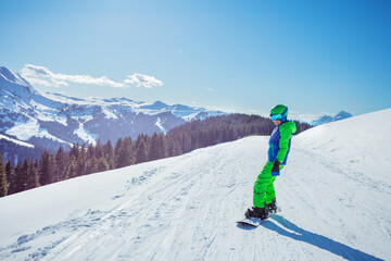 Fototapeta Boy in ski outfit stand on snowboard, sunny view over mountains obraz