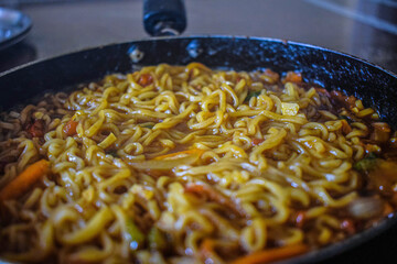Stock photo of delicious homemade hot and spicy noodles with vegetables,spices and herbs kept in frying pan. Picture captured under natural light at Bangalore, Karnataka, India. focus on object.