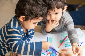 twin children painting with colored pencils and paints