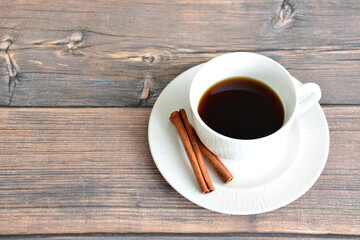 cup of coffee with cinnamon sticks isolated on wooden background