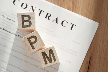 Wooden cubes with text BPM - short for business process managementon - on paper contract on the office table. business concept.