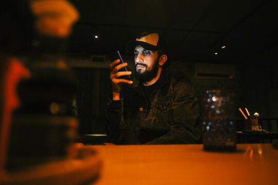 Caucasian bearded man using mobile phone in cafe at the night.