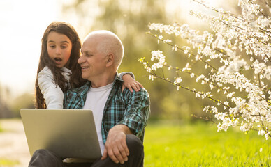 grandfather and granddaughter with laptop in the garden