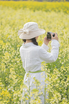 A girl in white with a hat is taking pictures in a rape field