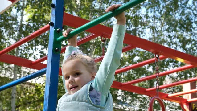 Active little girl climbing on monkey bars. Healthy activity for children. Child playing on outdoor playground.