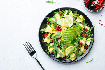 Summer vegan salad with juicy pineapple, fresh arugula, avocado and dried cranberry on white stone kitchen table, top view. Healthy eating, clean diet food, weight loss concept