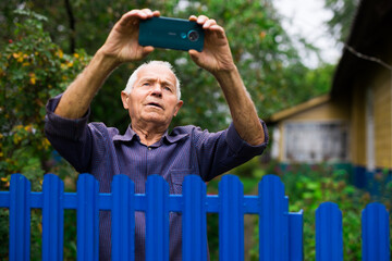 Old man with smartphone taking photographs outdoors