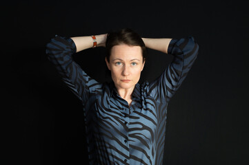 a portrait of a young woman holding her hands behind her head on a black background