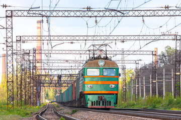 A green locomotive with a long freight train is going to the railway station. Freight railway transportation of goods.