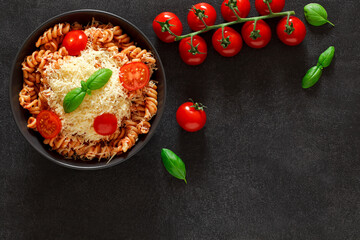 Pasta fusilli cooked with tomato sauce, basil, grated parmesan and branch of cherry tomatoes, top view, space to copy text.