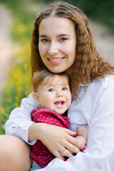 A smiling mother holds her little son in her arms while sitting in the park. Happy motherhood