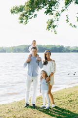 Summer portrait of a beautiful young family with two children near the lake. Mom, dad, son and daughter