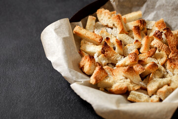 Crackers, dried baked pieces of white bread on craft paper on dark background, selective focus.