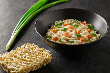 Noodles instant with vegetables in gray bowl on a dark background, selective focus.