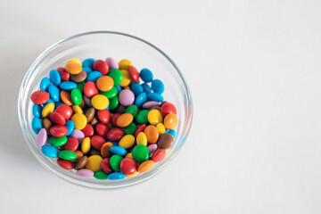 A lot of colorful round candies, taken in close-up, a vase with pills shifted to the left