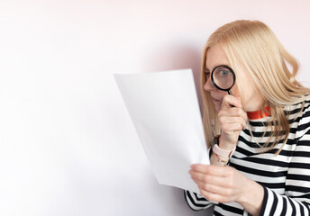 Funny mature woman  standing isolated over light background, reading document with magnifying glass