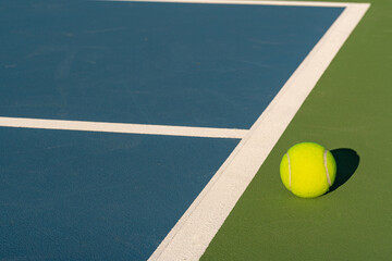 Yellow tennis ball at blue tennis court with white baseline and green out of bounds