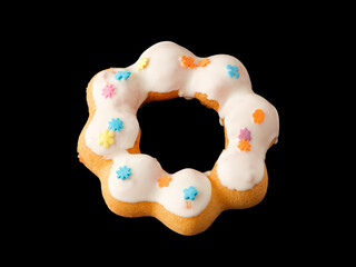 Cookies in the form of a ring in glaze and confetti on a black background.