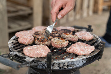 Man making barbecue, meatballs grilling on a portable barbecue outdoors in his garden.